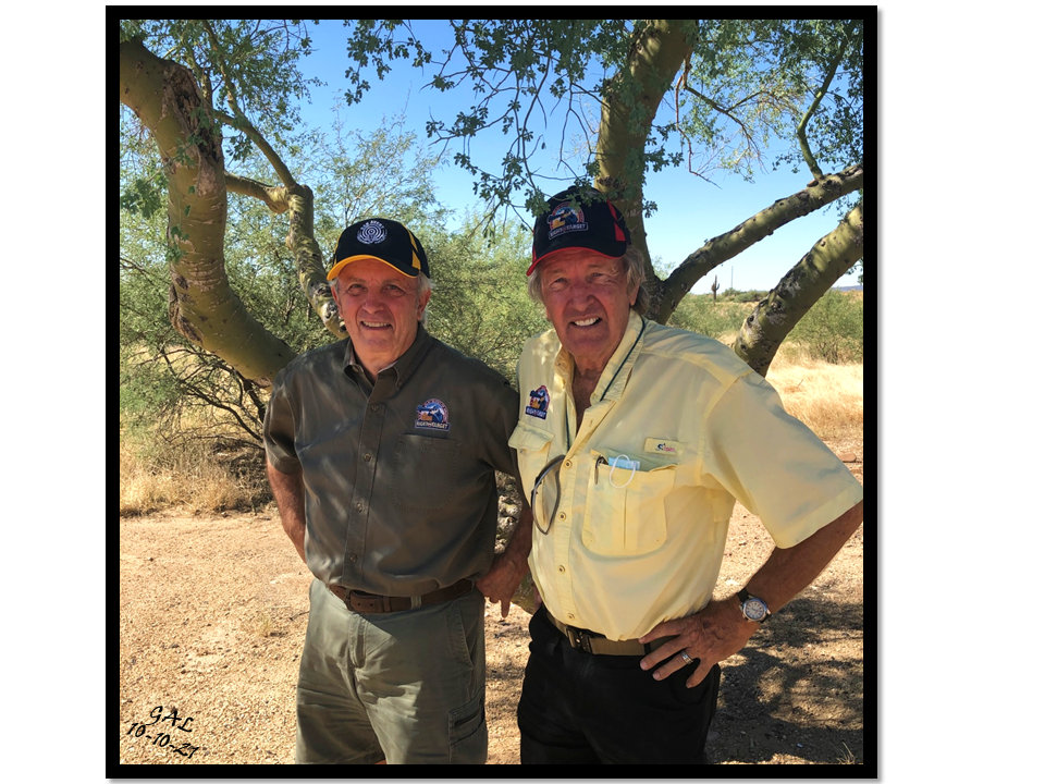 Two men standing next to each other under a tree.